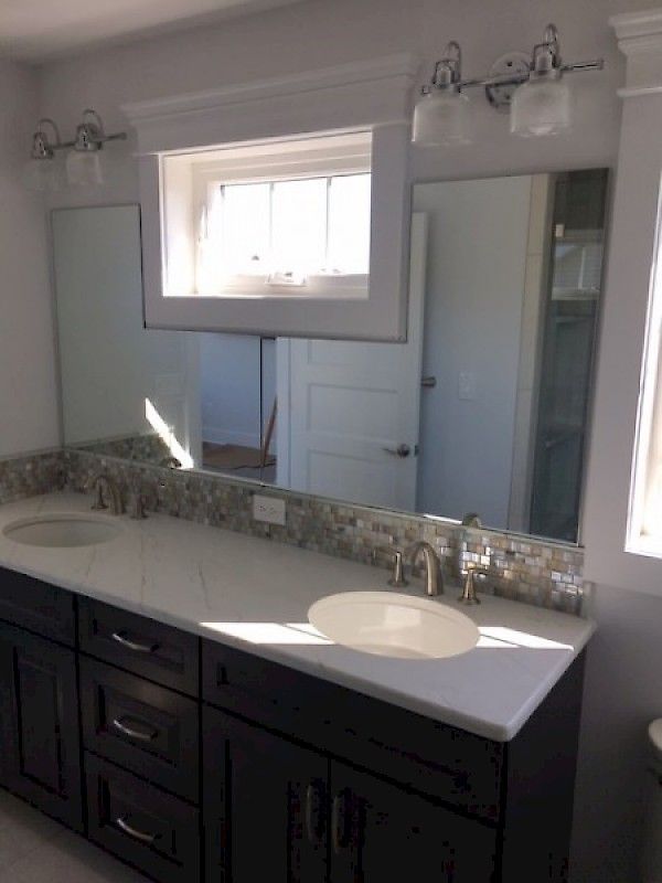 A modern bathroom vanity with dark cabinets, a white countertop, two sinks, mirrors, and light fixtures.
