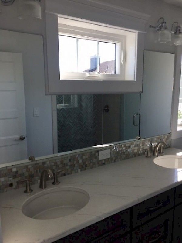 Bathroom vanity with a white quartz countertop, dual sinks, mosaic tile backsplash, a large mirror, and a window above.