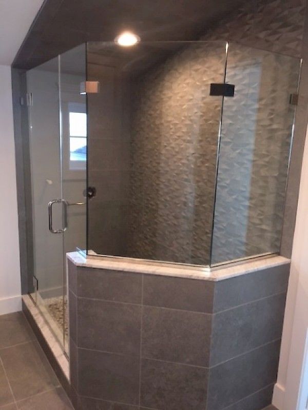 A glass-enclosed shower with a marble curb, gray tile base, and textured stone wall in a modern bathroom.