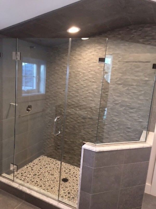 A walk-in shower with textured grey tile walls, a pebble-stone floor, and a glass door enclosure.