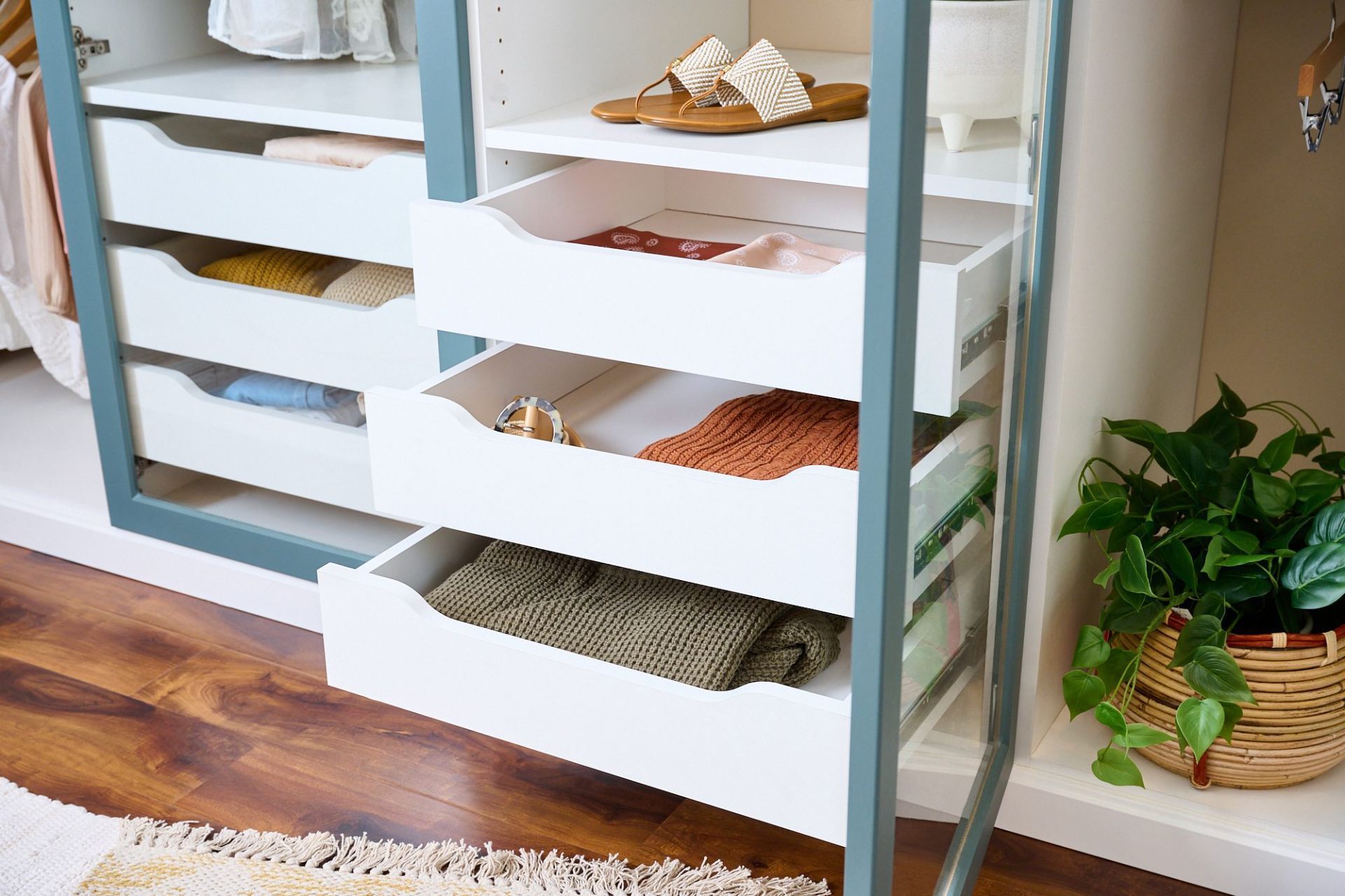 A modern, organized walk-in closet with white shelves, drawers, and hanging space, with dark brown accents and clothes.