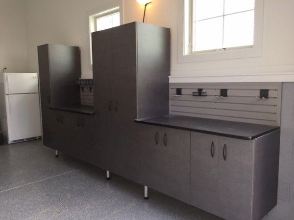 Dark gray storage cabinets with a countertop and wall-mounted track system in a garage next to a white refrigerator.