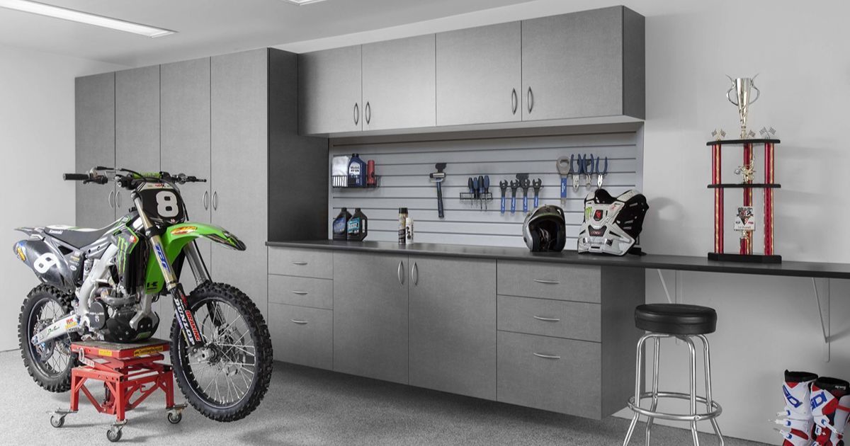 A garage featuring gray cabinetry, a slatwall, a trophy, and a green dirt bike on a red stand.