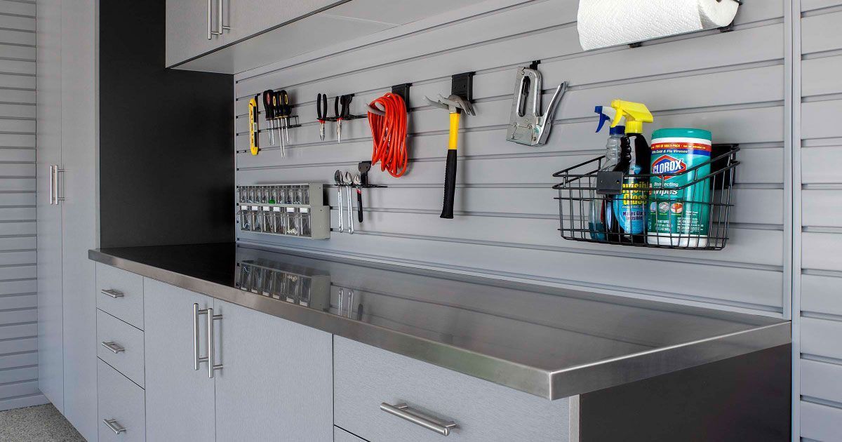 A modern garage workspace featuring gray cabinets, a metallic countertop, and wall-mounted storage panels holding tools.