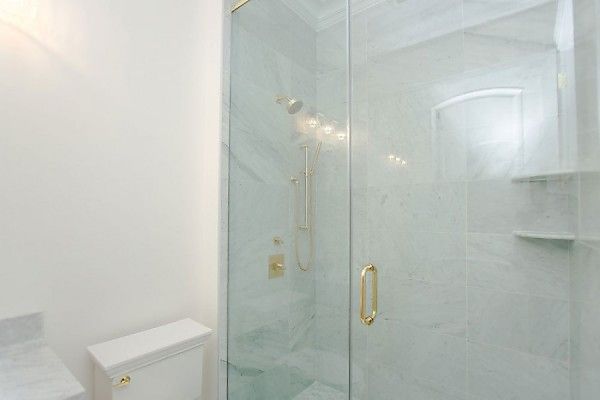 Modern white bathroom with a glass shower enclosure, gold fixtures, and marble-tiled walls.