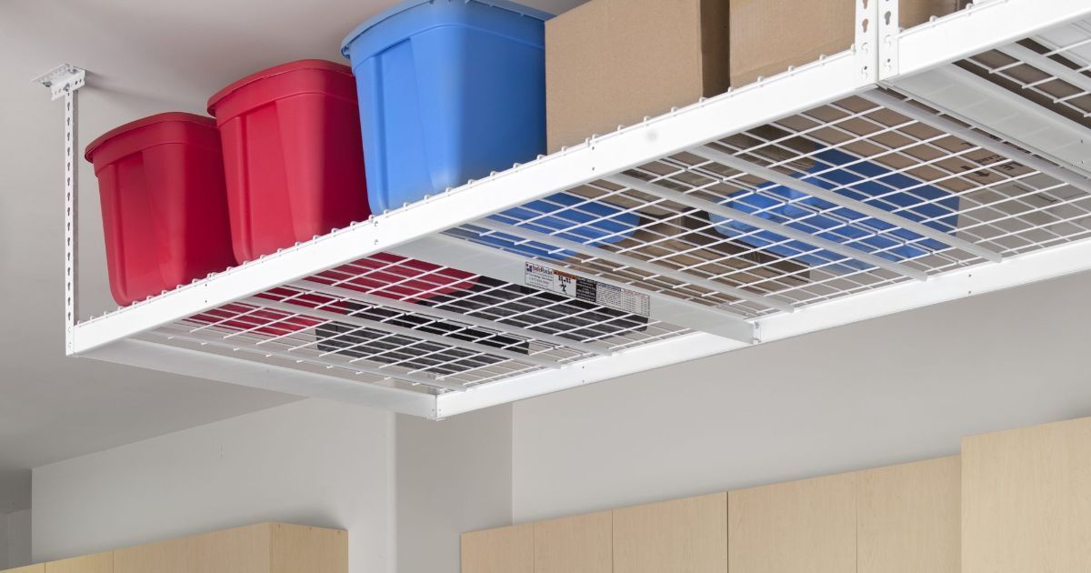 A white ceiling-mounted storage rack holds red and blue plastic bins and cardboard boxes above wooden cabinets.