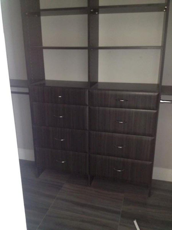 Two dark wood closet units, each with four drawers and open shelving above, standing on a matching wood floor.