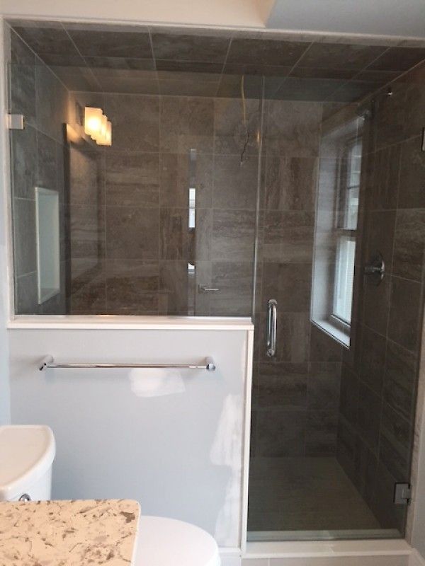 A modern walk-in shower with dark brown tile walls, a glass door, and a light-colored half-wall with a towel rack.