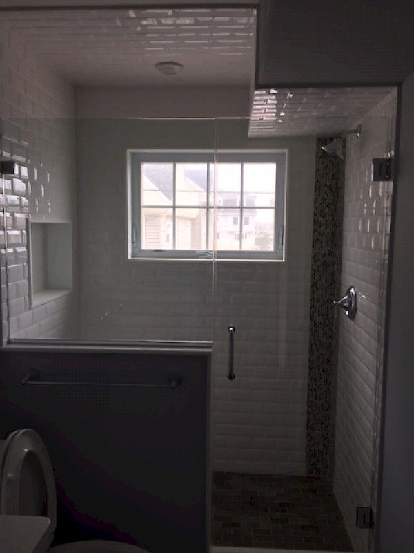 A walk-in shower with white subway tile walls, a glass door, a built-in recessed shelf, and a dark tiled floor.