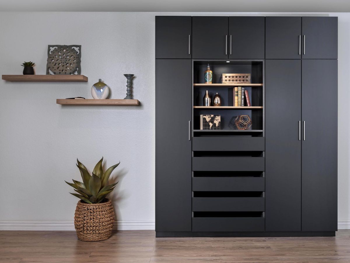 A modern, organized walk-in closet with white shelves, drawers, and hanging space, with dark brown accents and clothes.