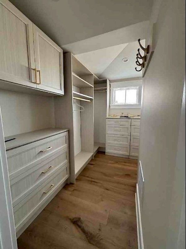 A walk-in closet featuring light-toned wooden cabinets, drawers, shelving, and matching hardwood flooring.