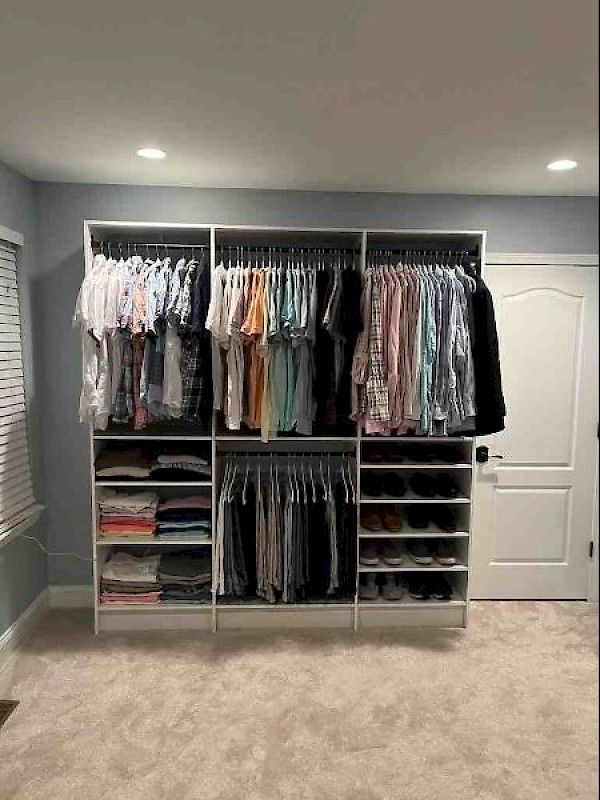 A large, organized white closet unit fills a wall, featuring hanging clothes, folded items on shelves, and shoe storage.