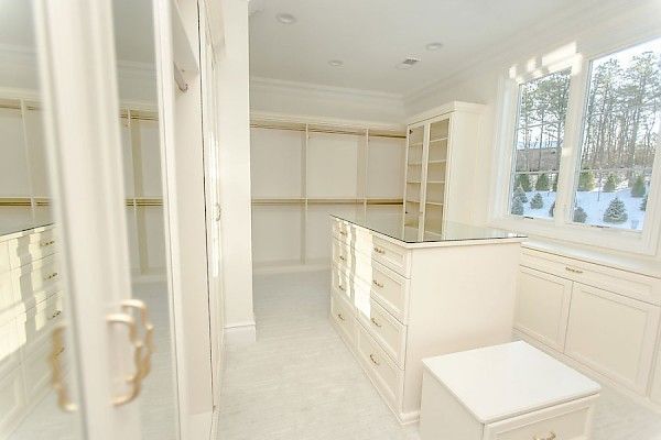 A bright, modern walk-in closet featuring cream-colored cabinetry, a central island with drawers, and a large window.