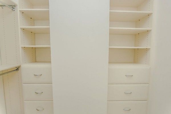 A closet interior featuring white built-in shelving and three drawers on both the left and right sides.