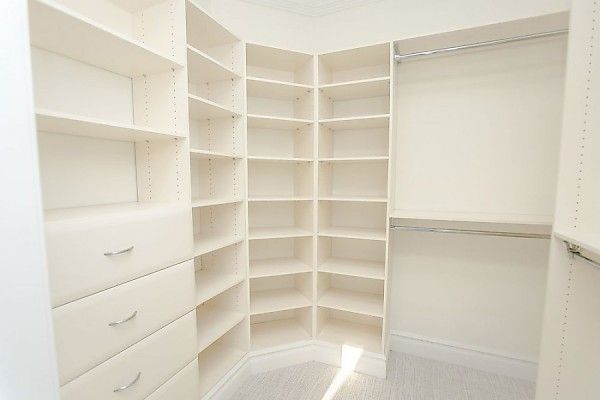 A walk-in closet featuring white wooden shelves, hanging rods, and a stack of three drawers against neutral walls.