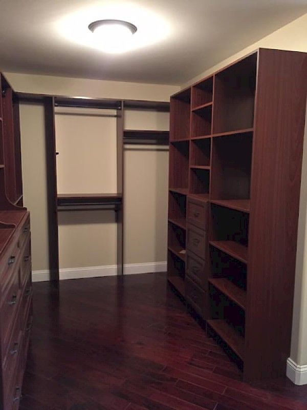 A walk-in closet featuring dark wood storage shelves, a built-in dresser, hanging rods, and dark hardwood flooring.