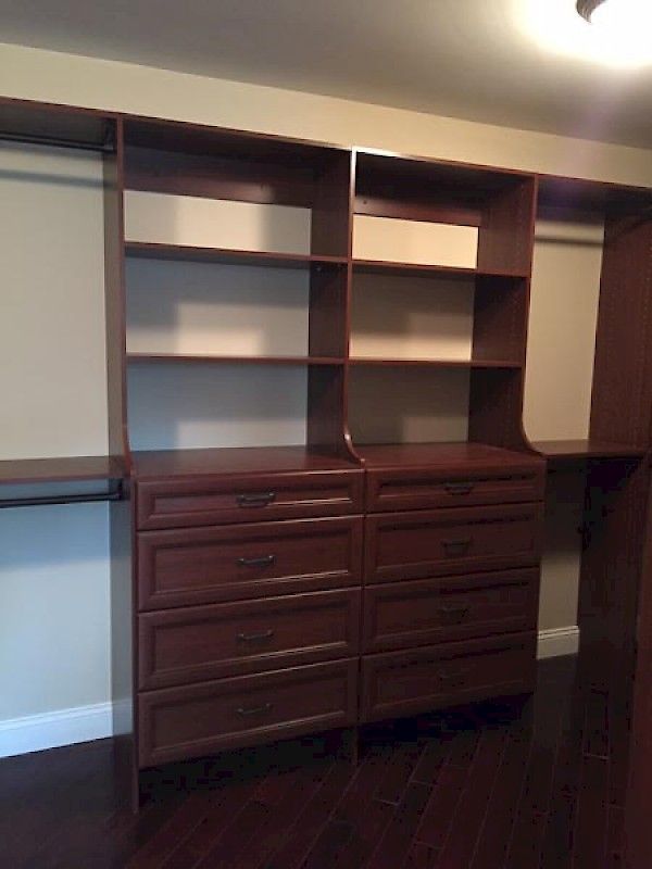 A custom dark wood closet system featuring two vertical towers of open shelves sitting atop four drawers each.