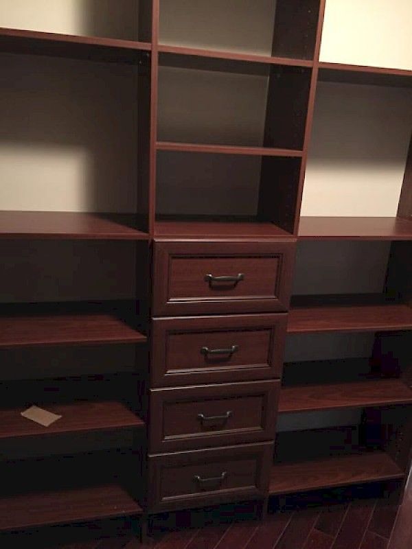 Dark wood shelving unit with a central column of four stacked drawers flanked by open shelves against a white wall.