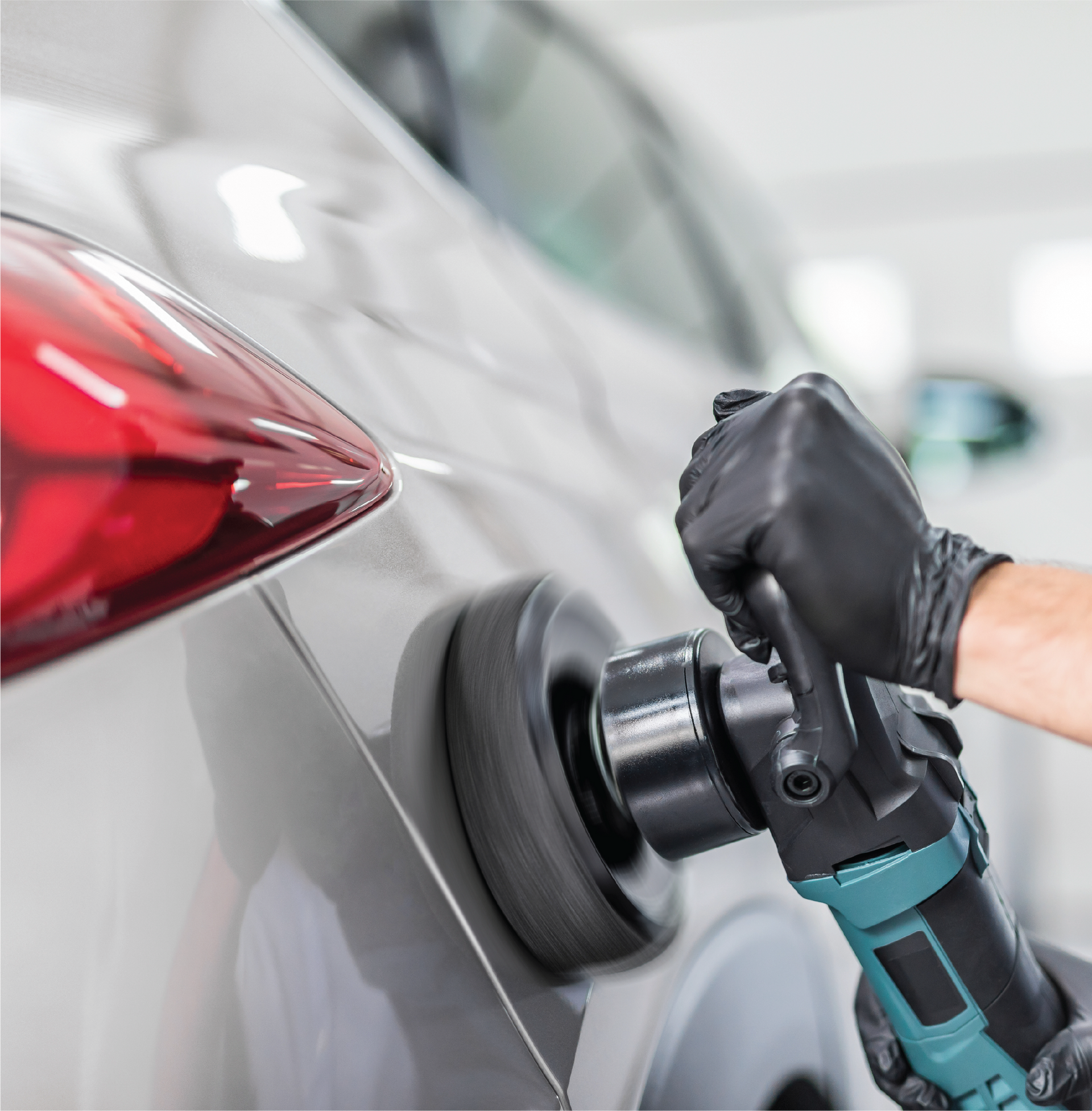 A man is polishing a blue car with a sander.