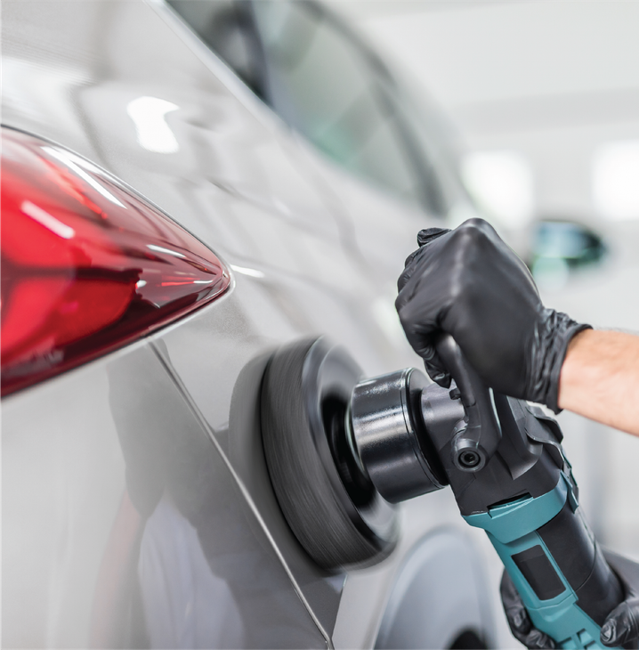 A man is polishing a blue car with a sander.