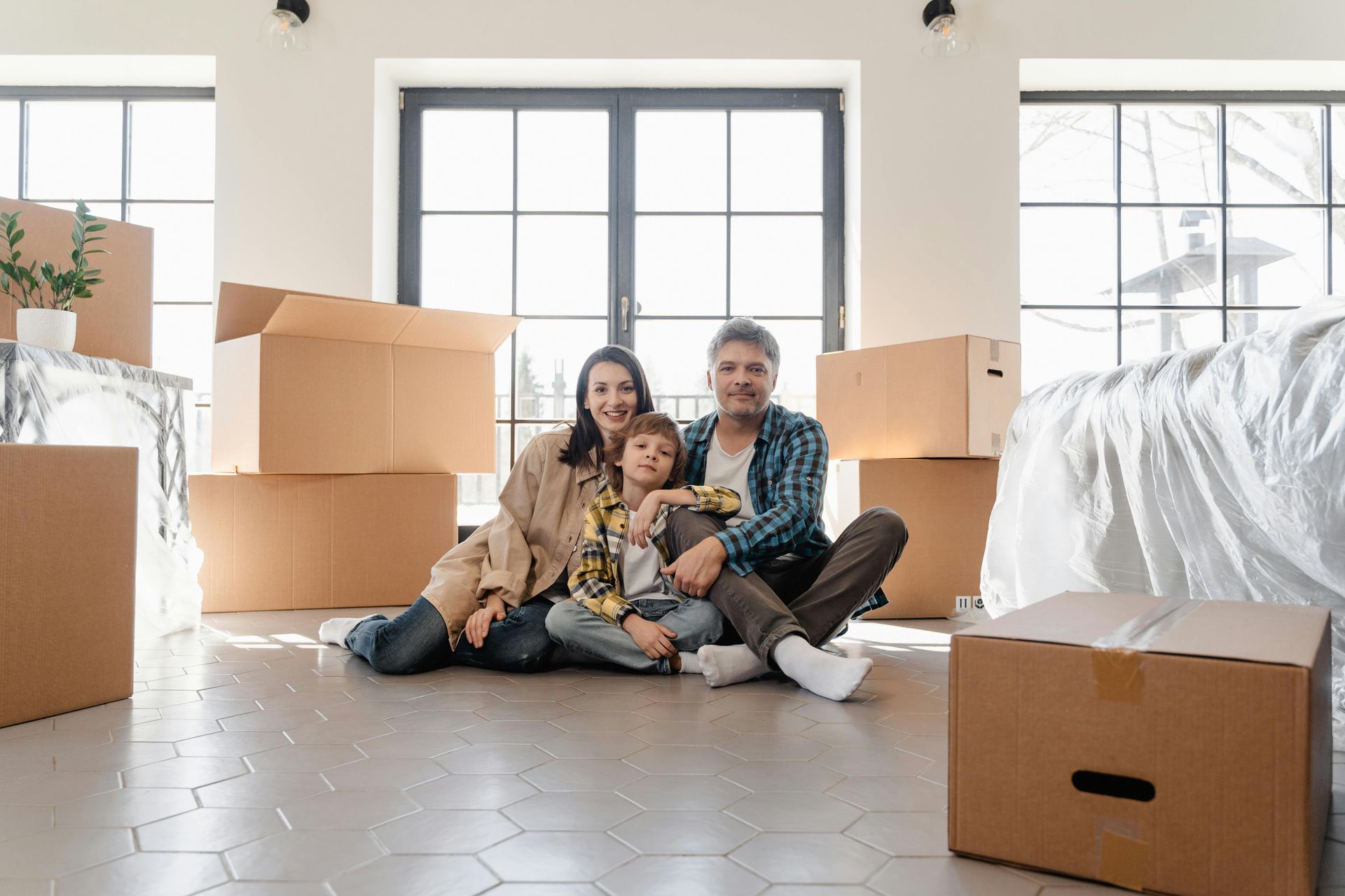 Family sitting among moving boxes... smiling during a home move, with rodent control treatment being performed in the background