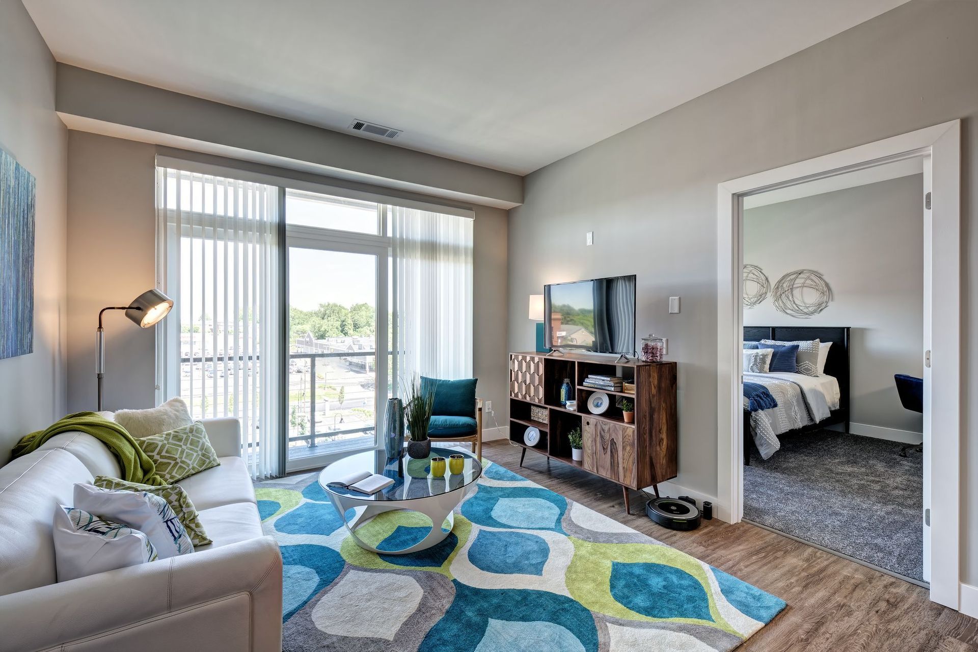 A living room with a couch , table , rug and sliding glass doors leading to a bedroom.