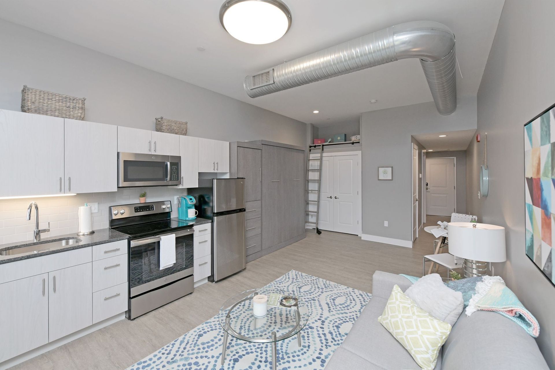 A living room with a couch and a kitchen with stainless steel appliances.
