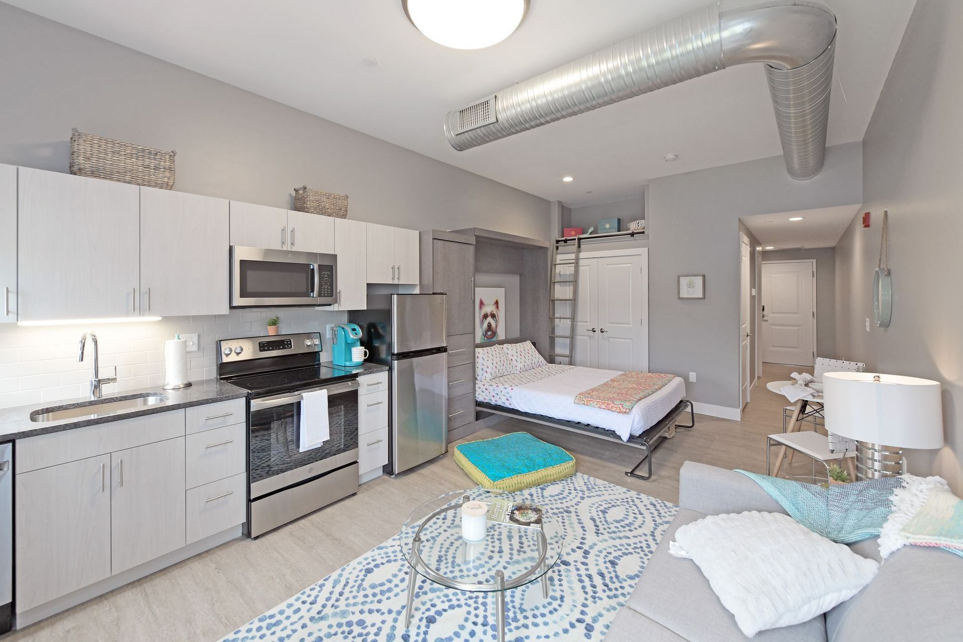 A living room with a couch , a bed , a kitchen and a refrigerator.