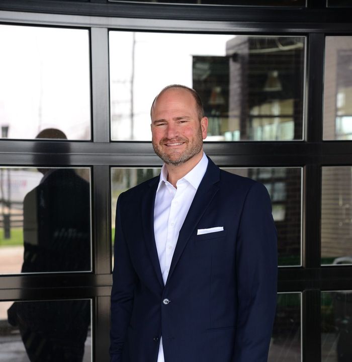 A man in a suit is standing in front of a window