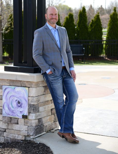 A man in a suit and jeans is leaning against a stone pillar.