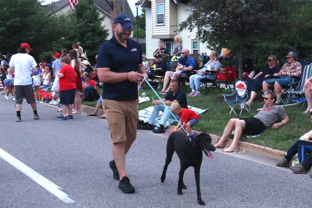 A man is walking a dog on a leash in a parade.