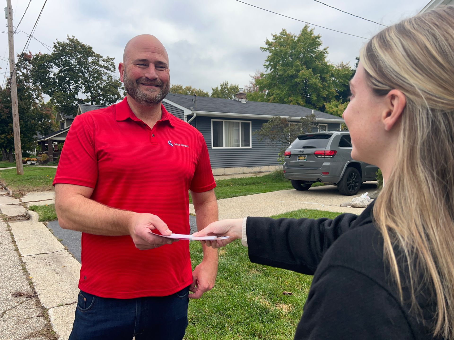 A man in a red shirt is handing a piece of paper to a woman.