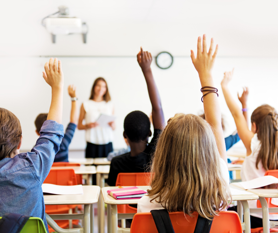 A group of children are raising their hands in a classroom to answer a question.