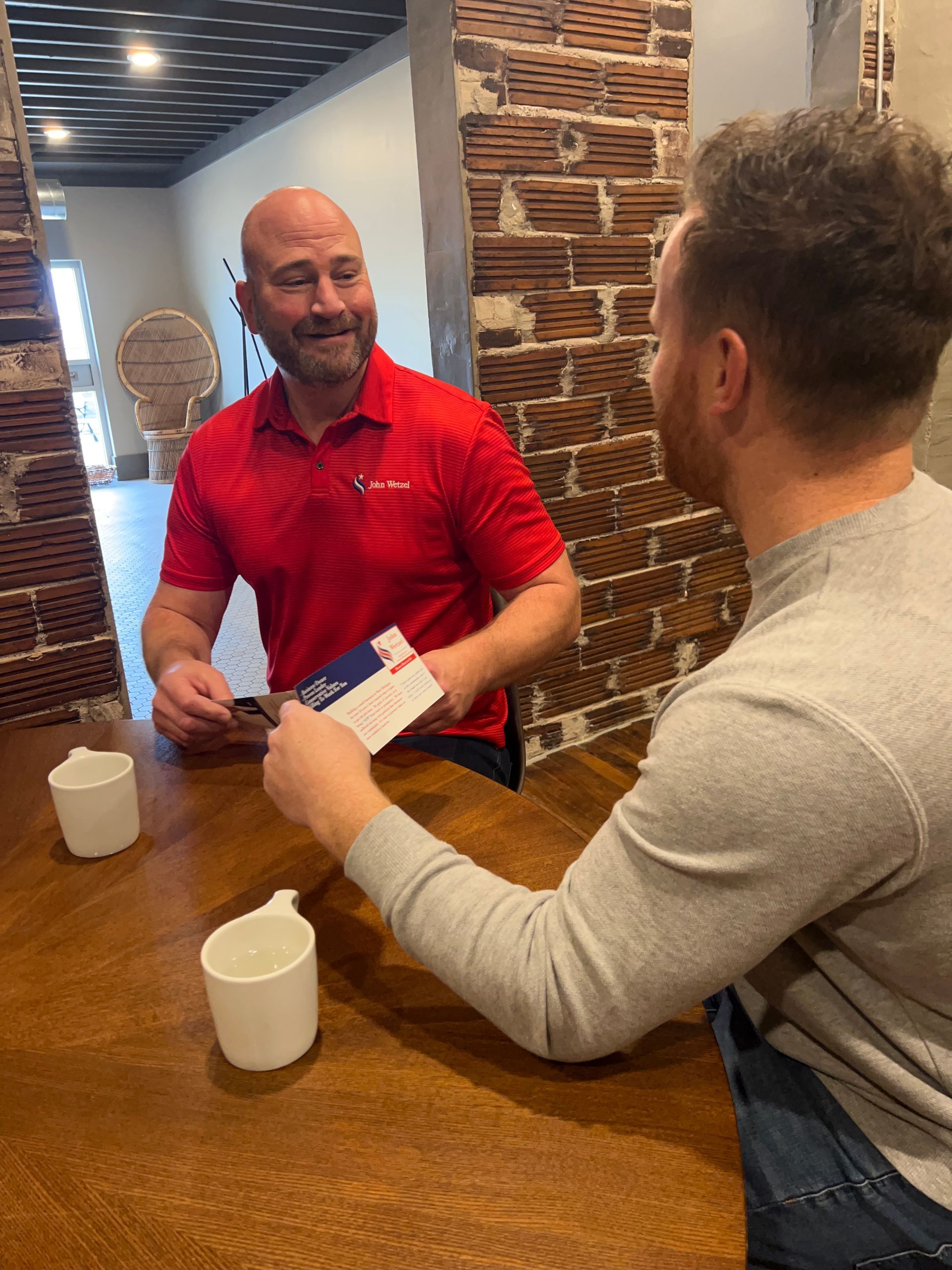 Two men are sitting at a table talking to each other.