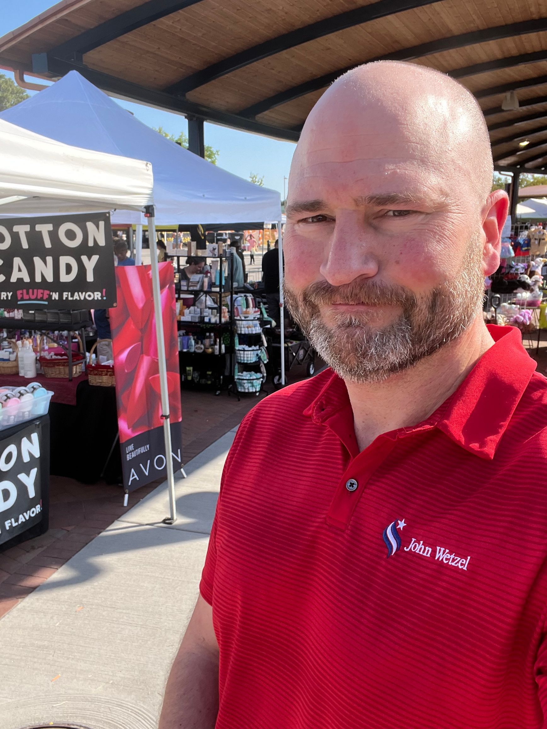 A man in a red shirt is standing in front of a cotton candy stand.