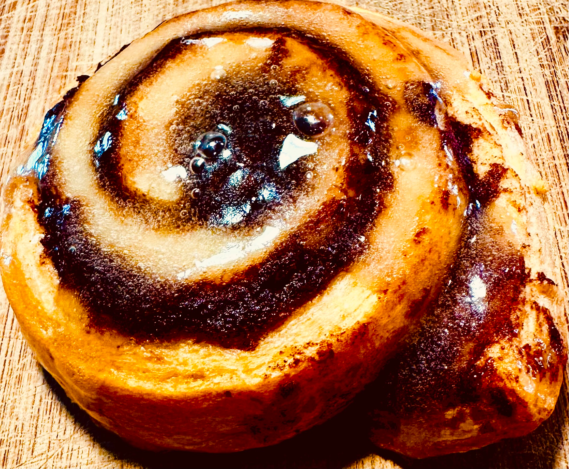 Cinnamon roll with dark brown swirl filling and glazed top on a wood surface.