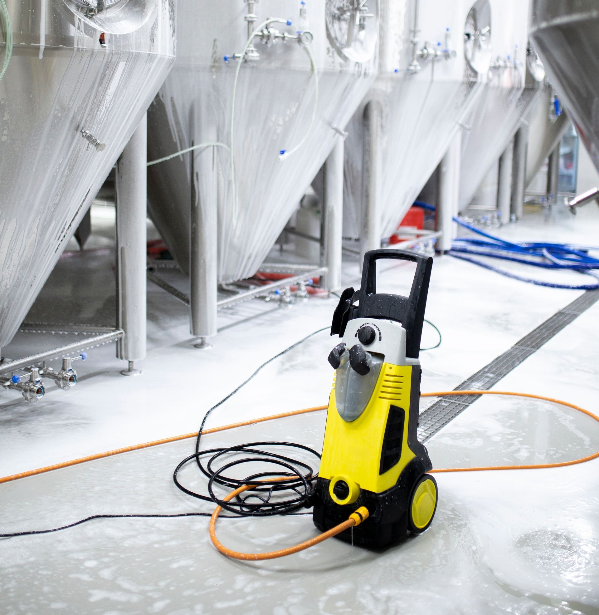 Pressure washer cleaning brewery floor, tanks in background.