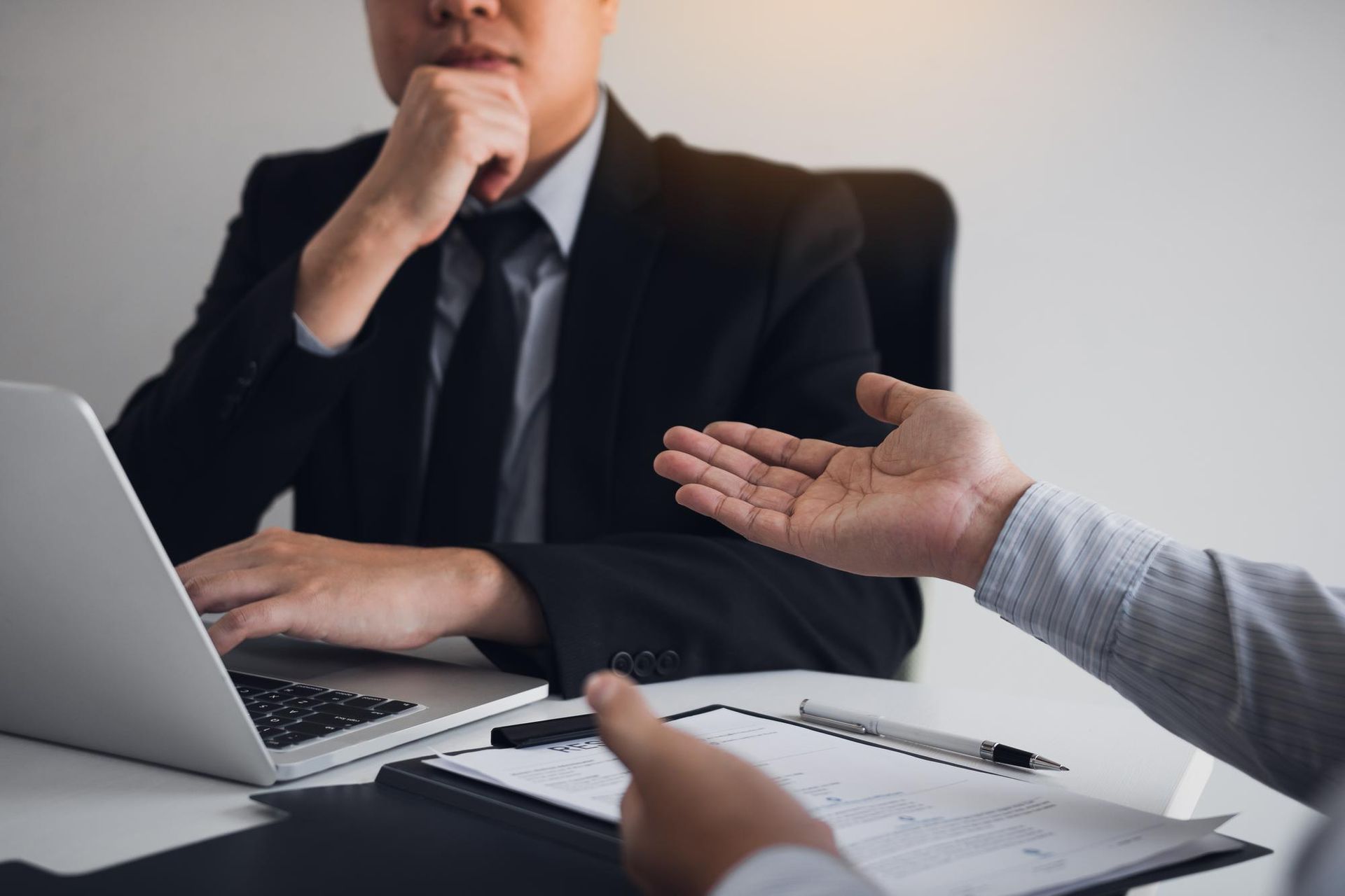 Two professionals in business attire discuss work at a desk with a laptop and documents.