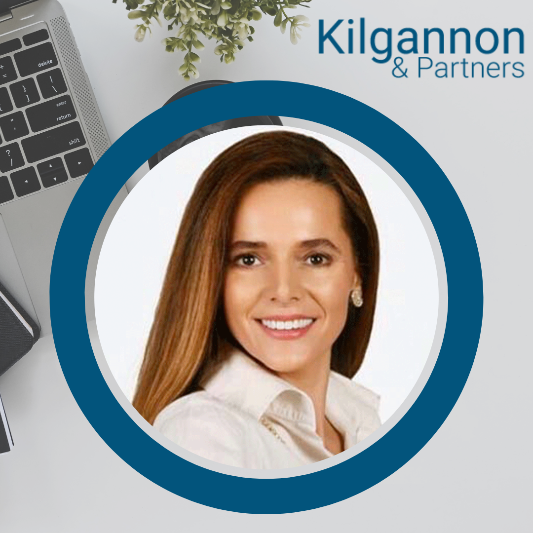 A smiling woman in a white collared shirt, centered within a blue circular frame against a professional office backdrop.