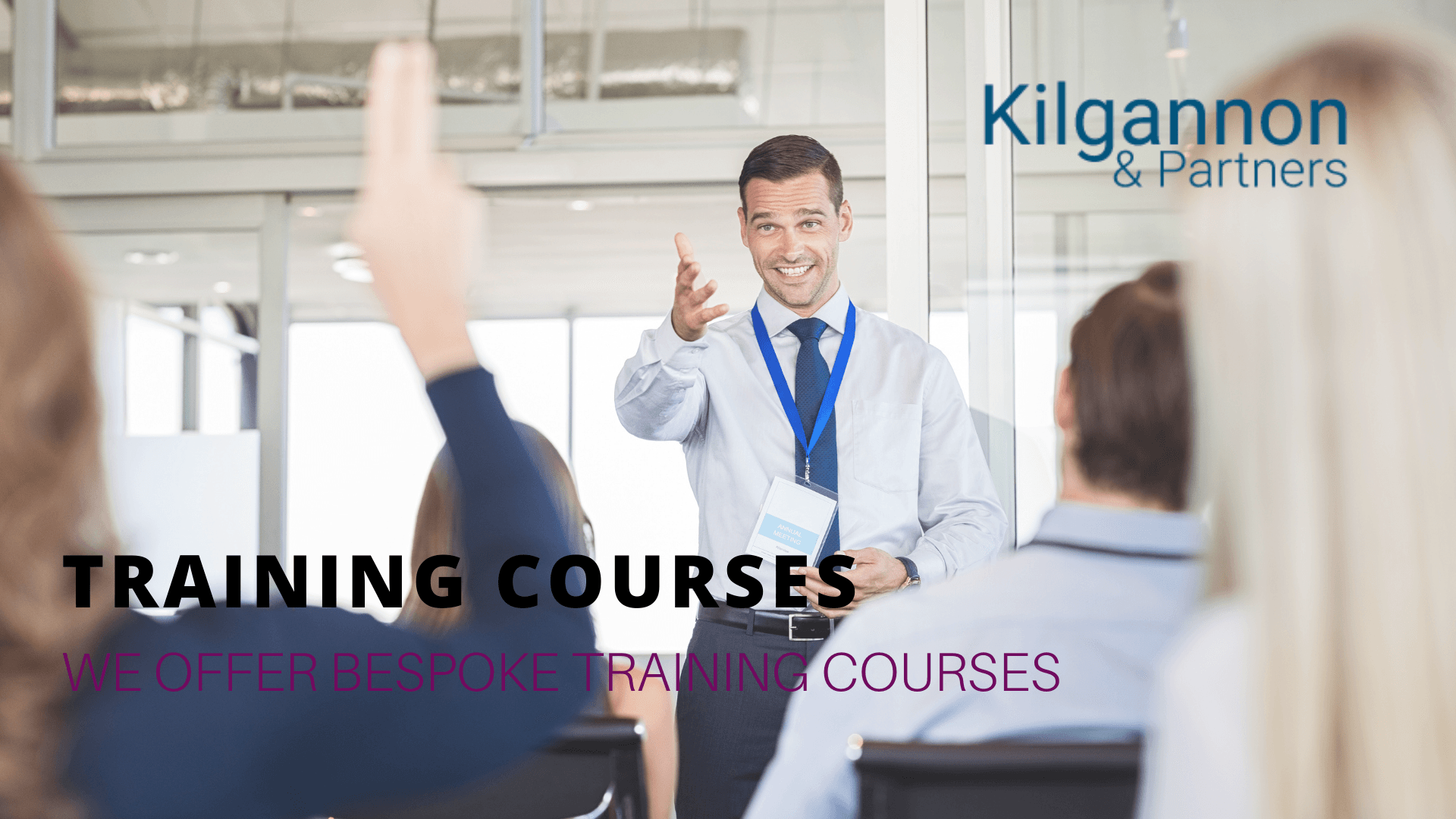 A business professional conducts a training session for a seated group as one attendee raises their hand.