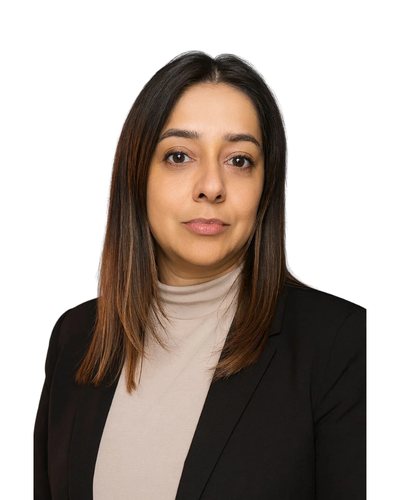 A professional headshot of a person with long dark hair, wearing a beige mock-neck top and a black blazer, white background.