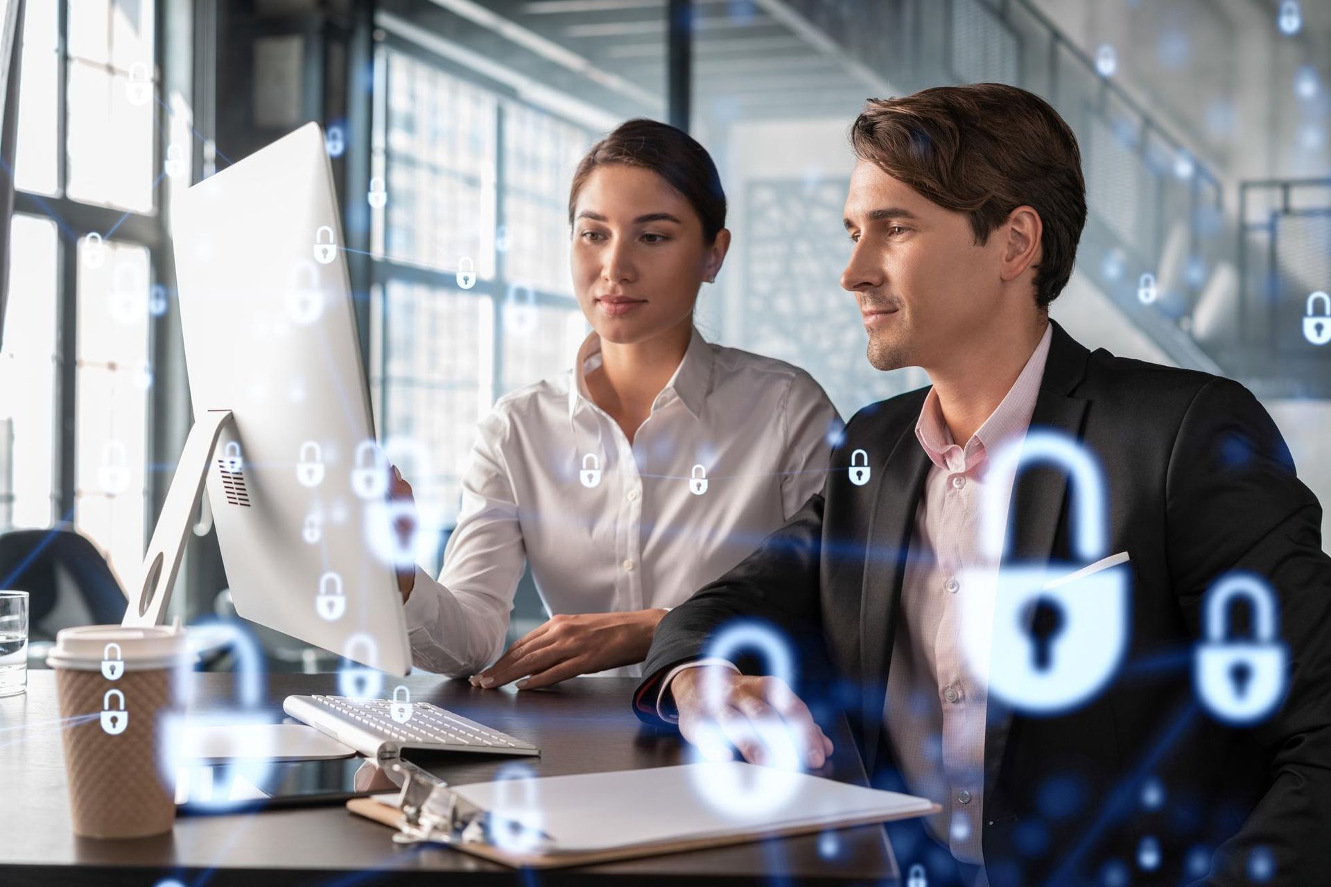 Two professionals working at a computer in an office, surrounded by glowing digital padlock icons representing data security.