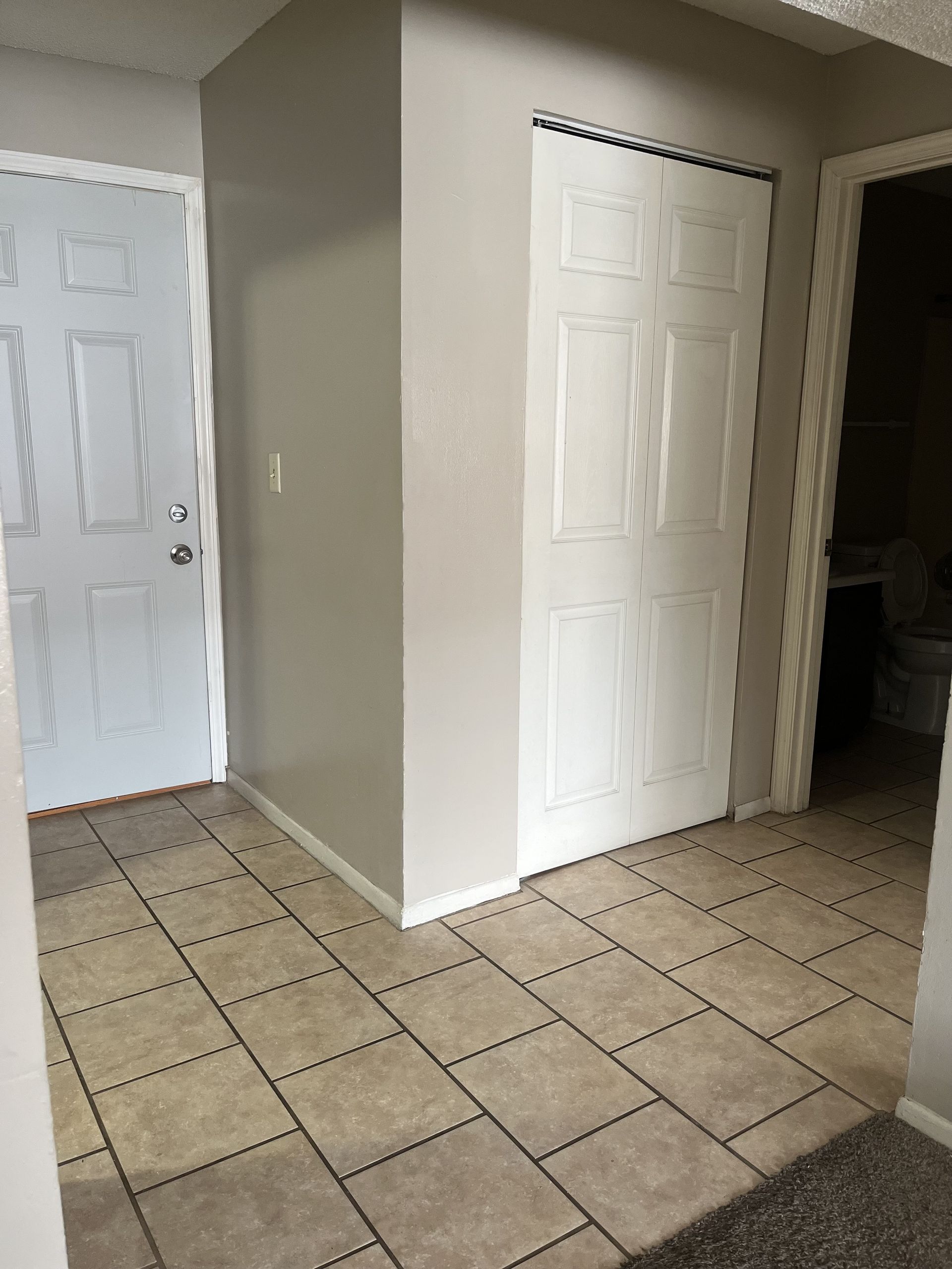 Hallway with tiled floor, white door and closet, off-white walls.