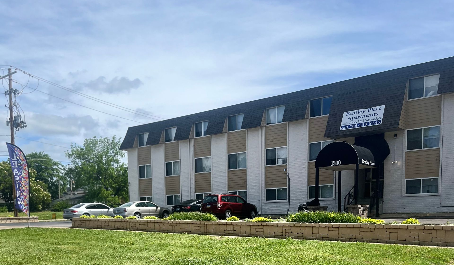Apartment building with cars parked out front, on a sunny day.