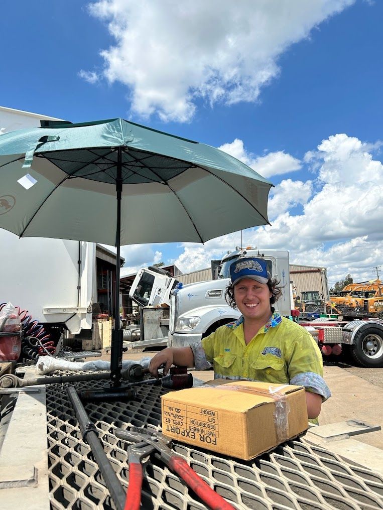 A Man is Sitting at a Table Under an Umbrella With a Box on It — Trucks On The Run Pty Ltd in Glenvale, QLD