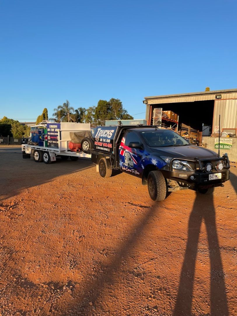 A Truck is Being Towed by a Trailer in a Dirt Field — Trucks On The Run Pty Ltd in Clifton, QLD
