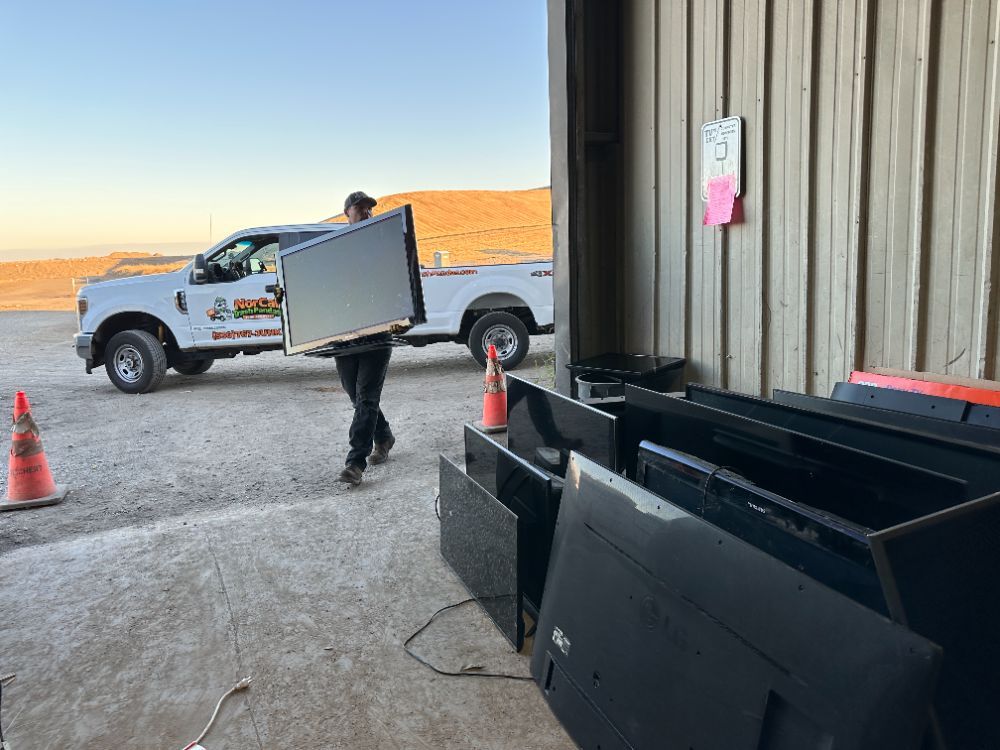 A person wearing yellow gloves is holding a cell phone in front of a pile of old cell phones.