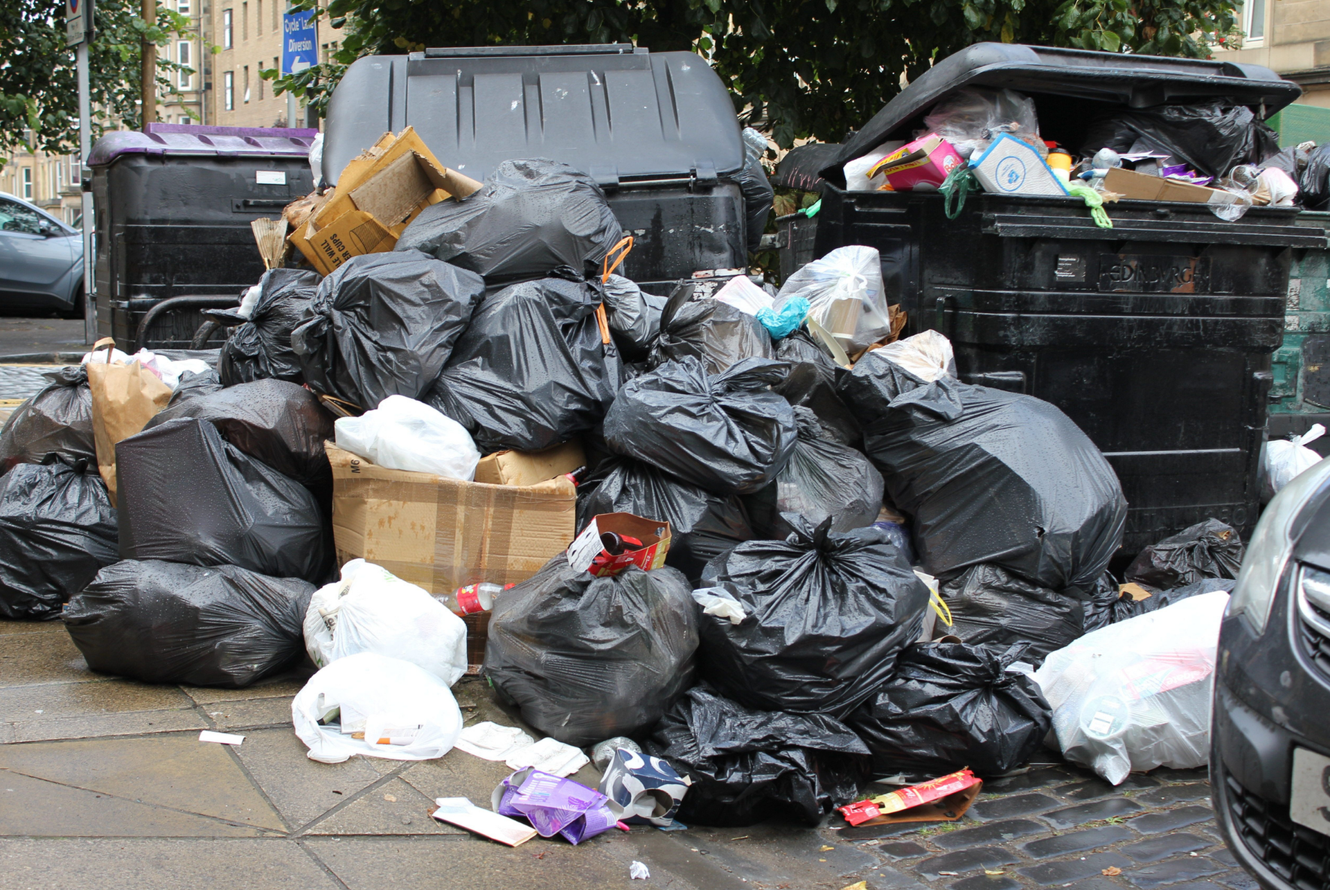 A pile of garbage is sitting on the sidewalk in front of a dumpster.