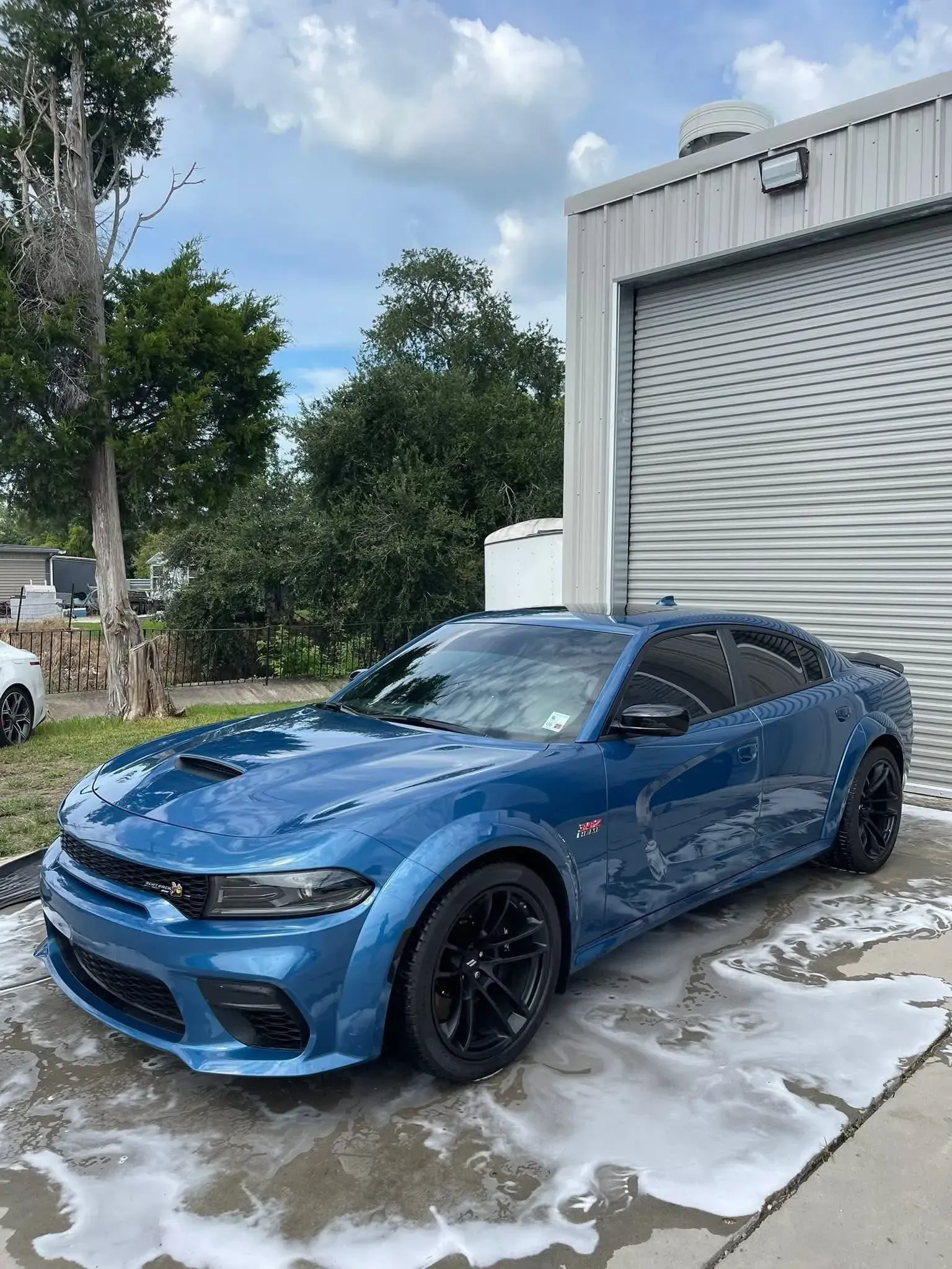 Blue Dodge Charger parked outside a building with its wheels and body covered in soap.