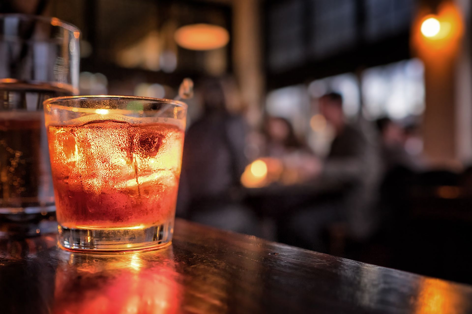 Cocktail in a glass with ice on a bar. Blurred background of people in a dimly lit bar.